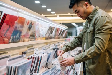 Side view of crop concentrated male customer picking new vinyl record placed in rows on shelves in mall