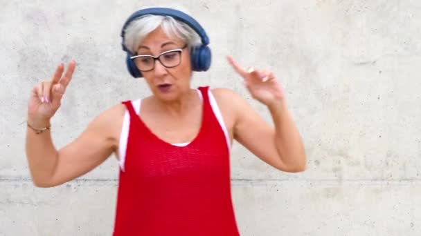 ワイヤレスヘッドフォンのハッピーシニア女性は音楽を聴き 屋外で踊っています 高品質のフルHd映像 — ストック動画