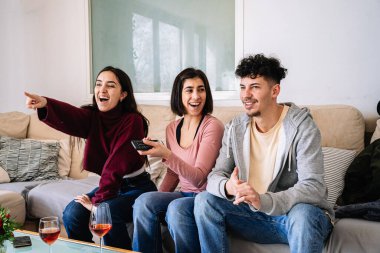Üç arkadaş birlikte televizyon izlemekten zevk alıyorlar. Kanepede şarap kadehleri eşliğinde gülerek ekranı gösteriyorlar..
