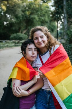 Gökkuşağı bayrağını tutarken birbirini kucaklayan iki kadın.