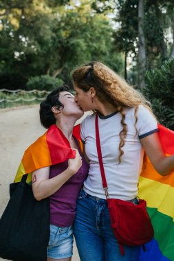 İki kadın öpüşüyor ve bir gay onur etkinliğinde gökkuşağı bayrağı taşıyor.