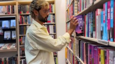 Genç adam rahat bir kitapçıda kitap seçiyor.