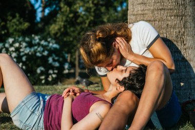 Parktaki bir ağacın yanında iki kadın öpüşüyor.