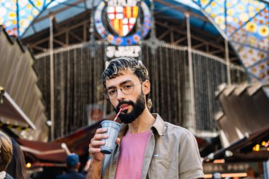 Genç adam Barselona 'daki ünlü Boqueria pazarında pipetle smoothie içiyor.