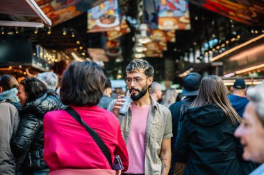 Kalabalık La Boqueria pazarında yürürken ve arkadaşlarıyla konuşurken şık bir adam smoothie içiyor.