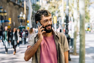 Yoğun bir caddede yürürken telefonla konuşan genç bir adam.