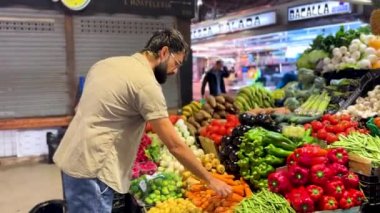 Markette renkli sebze gösterilerinden ürün seçen bir adam.