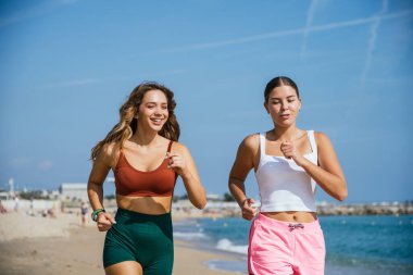 İki bayan sporcu sahilde koşuyor, güzel havanın tadını çıkarıyor ve sağlıklı bir yaşam tarzını destekliyor.