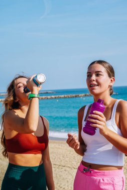 İki bayan sporcu sahildeki eğitimden sonra dinlenip su içiyorlar.