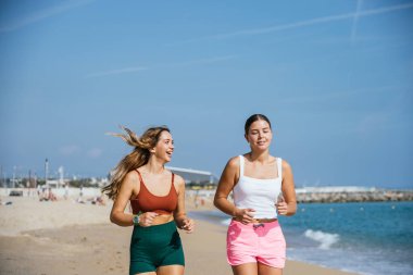 İki arkadaş güzel güneşli bir günde kumsalda koşuyorlar, temiz havanın ve deniz esintisinin tadını çıkarıyorlar.