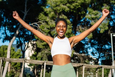 Parkta zaferi kutlayan, kollarını kaldırıp bağıran mutlu bir sporcu.