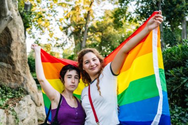 İki kadın parkta gökkuşağı bayrağı taşıyor. Igbt 'ın gurur ve eşitliğini simgeliyor.