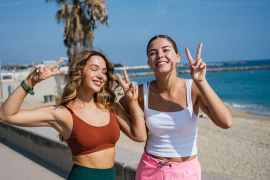 Yaz tatilinin tadını çıkarırken iki mutlu kadın parmaklarıyla barış işareti yapıyor.