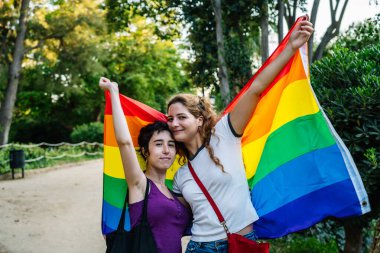 İki genç kadın parkta gökkuşağı bayrağı tutuyorlar. Igbt 'ın gurur ve çeşitliliğini kutluyorlar.