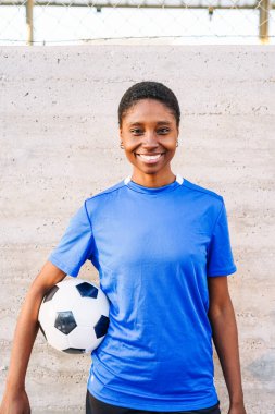 Mavi formalı, elinde futbol topu tutan gülümseyen bir sporcu.