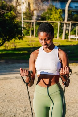 Güneşli bir parkta direniş bantlarıyla çalışan sağlıklı bir kadın.