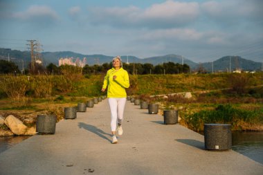 Aktif son sınıf öğrencisi kadın açık hava egzersizinden, nehir kenarındaki pitoresk bir parkta koşmaktan, sağlıklı bir yaşam tarzını kucaklamaktan hoşlanıyor.