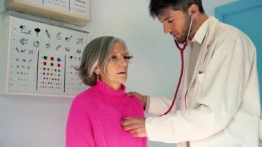 Doktor, yaşlı bir kadının göğsüne steteskop takıyor.