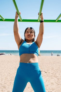 Güneşli bir günde plaj jında spor yapan Asyalı bir kadın.