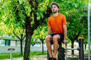 Genç sporcu, arka planda ağaçlar ve binalar olan bir parkta çukur kazarak sağlıklı bir yaşam tarzının tadını çıkarıyor.