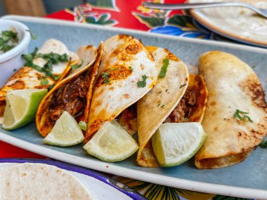 Kişniş ve limon dilimleri ile süslenmiş barbacoa tacolarının yakın çekimi, canlı ve iştah açıcı bir Meksika mutfağı deneyimi sergiliyor.
