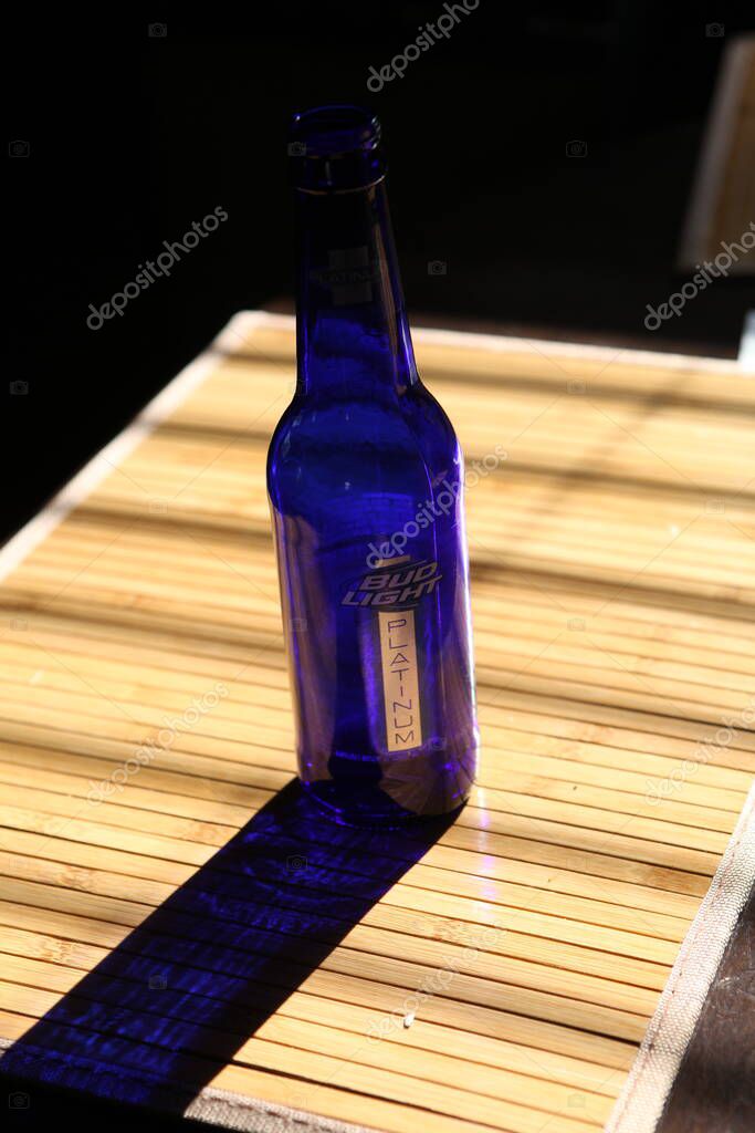 Columbus,Ohio July 5, 2020 Bud Light Beer Bottle drawing long shadows on a wood table.