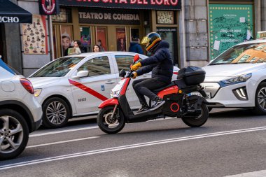 Electric motorcycle of the company acciona for rent by the minute driven along gran via street in madrid between several cars and cabs.