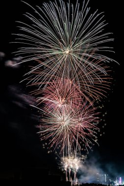 Vertical image of a fireworks show with pyrotechnics launched at different heights and many colors captured with long exposure.