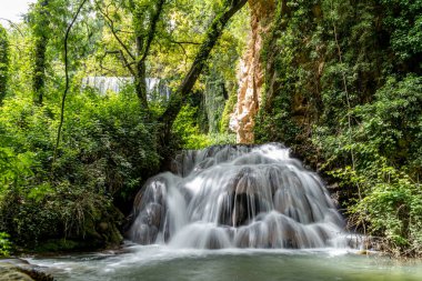 River with a cascade of multiple waterfalls in the middle of nature surrounded by trees and green vegetation, with long exposure and silk effect.