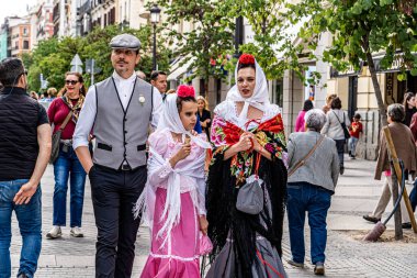 Madrid, İspanya. 15 Ağustos 2023. Sokakta yürüyen bir ailenin dikey görüntüsü Chulapos kostümleri giymiş San isidro şenlikleri için tipik Madrid şehri..