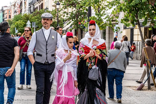 Madrid, İspanya. 15 Ağustos 2023. Sokakta yürüyen bir ailenin dikey görüntüsü Chulapos kostümleri giymiş San isidro şenlikleri için tipik Madrid şehri..