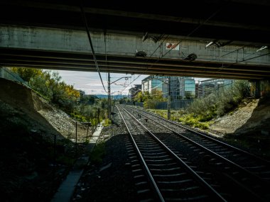 Tren raylarından yüzeye çıkan bir metro tüneline çıkıyor. Güneşli bir gün ve arka planda beyaz bulutlar var.. 