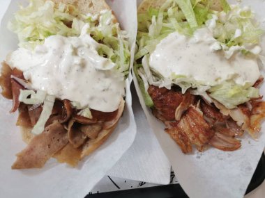 İki kebap yakın çekim, biri sığır etli, diğeri tavuklu, yoğurt soslu ve marullu, Pide ekmeğine sarılmış ve kağıt torbalara servis edilmiş, yemeye hazır..