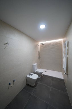 Modern banyo tadilatı bitmek üzere. Özellikleri bide, tuvalet, duşa girme, asma tavan ve LED ışıklandırma. Lavabo ve ayna henüz kurulmadı. Tarafsız tonlar ve parlak tasarım.