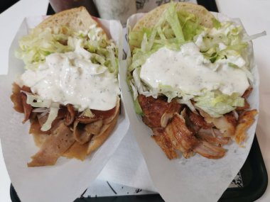 İki kebaplı kâğıt ambalaj, biri tavuklu ve biri biftekli. Marul, beyaz sos ve pide ile servis edilir. Arka planda sos şişeleri olan sokak yemekleri sunumu.