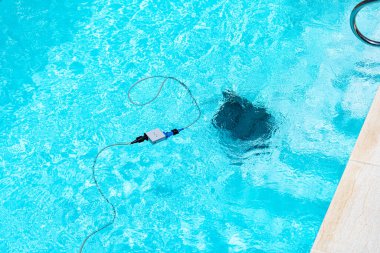 Temiz mavi bir havuzun havuzu ve hareket halindeki bir robot temizleyicisi. Beyaz fayanslarla, yeşil sentetik çimlerle ve güneşli bir günde metal merdiven ile çevrili..