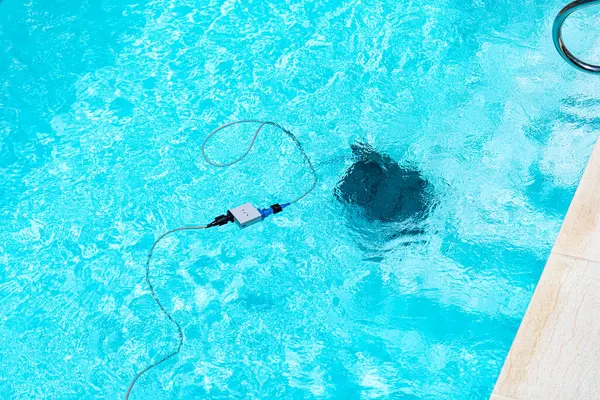 Temiz mavi bir havuzun havuzu ve hareket halindeki bir robot temizleyicisi. Beyaz fayanslarla, yeşil sentetik çimlerle ve güneşli bir günde metal merdiven ile çevrili..