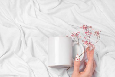 Kadın elleri, tekstil arka planında boş bir kupanın bir kopyasını tutar. Tasarım ve logo için yakın plan bir fincan. Sevgililer Günü için kırmızı kalpli beyaz manikür tırnakları..