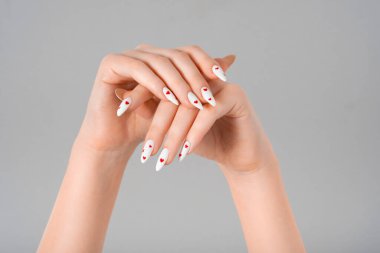 Kadın manikürü, iki el en az jel cilası, beyaz uzun tırnaklar ve izole edilmiş gri arka plan, kırmızı kalpler. Güzellik merkezi, Sevgililer Günü, aşk konsepti