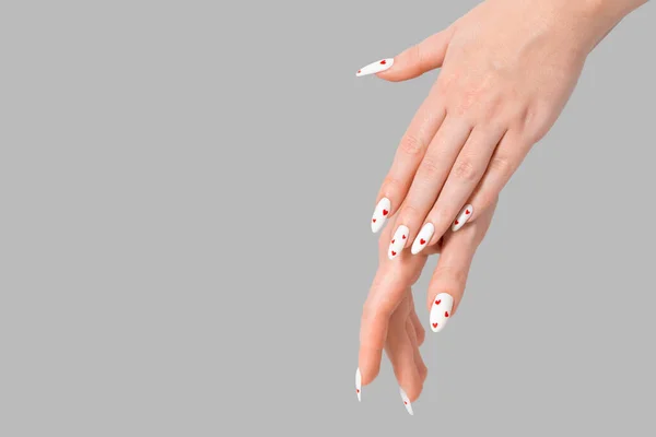 Female manicure two hands minimal gel polish white long nails and red hearts desing gray isolated background. Beauty spa, Valentine's Day, love concept