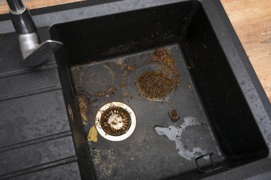 Dirty granite kitchen sink black with leftover bits of food. Before. House cleaning service.