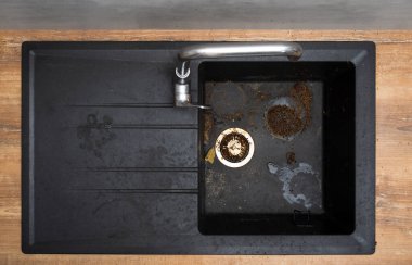 Dirty granite kitchen sink black with leftover bits of food. Before. House cleaning service.