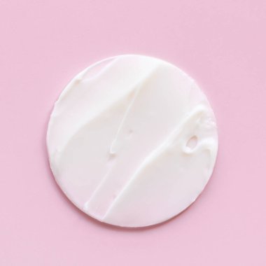 İzole edilmiş açık pembe arka planda beyaz krem dokusu, yüz ve vücut için kozmetik. Döndür.