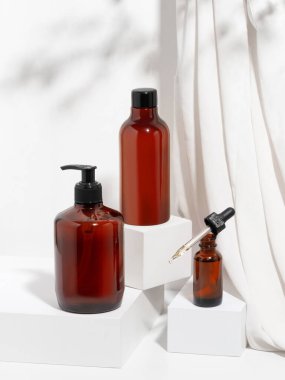 Ceset için bir takım kozmetik ürünler, banyo. Kahverengi duş jeli ya da sıvı sabun, krem ve vücut masajı şişelerinin beyaz arka planda geometrik podyum ile modellenmesi