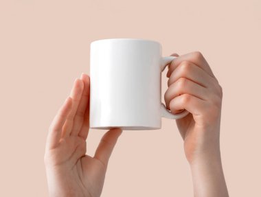 Kadın eli, beyaz bir seramik kupa tutuyor. Bej izole bir arka planda, fotokopi alanı olan bir kahve fincanı. Tasarım, markalaşma ve iş için boş şablon