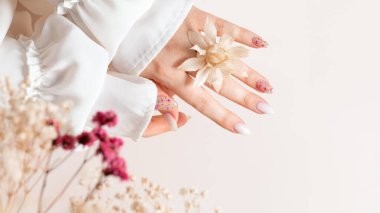 Beyaz jel cilası ve kurumuş çiçek desenli kadın ellerinin bahar manikürü. Dişi eller, bej arka planda beyazlatılmış kurumuş safran çiçekleri tutar..