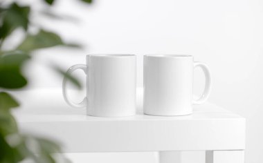 Mockup of a white tea cup or coffee mug on a white table in a Scandinavian style kitchen with a houseplant Scheffler plant. Subject template for your design, advertising with copy space clipart