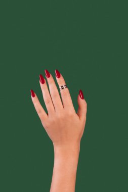 Kadın elleri gevşemiş, zümrüt yeşili arka planda kırmızı jel ojeli uzun tırnaklar. Klasik bir manikür ve gümüş yüzük seti olan bir kadın.