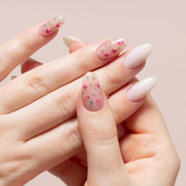 Beyaz jel cilası ve kurumuş çiçek desenli kadın ellerinin bahar manikürü. Bej bir arkaplanda kadın elleri