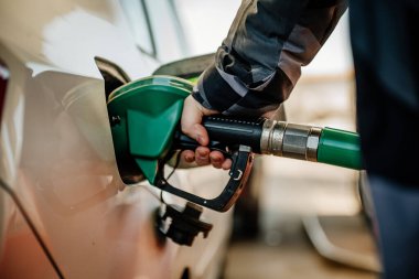 Benzin istasyonunda arabaya benzin dolduran biri.